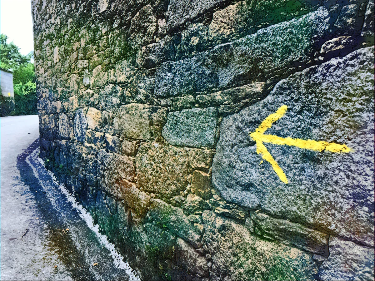 Ein gelber Camino-Pfeil auf einer Steinmauer.