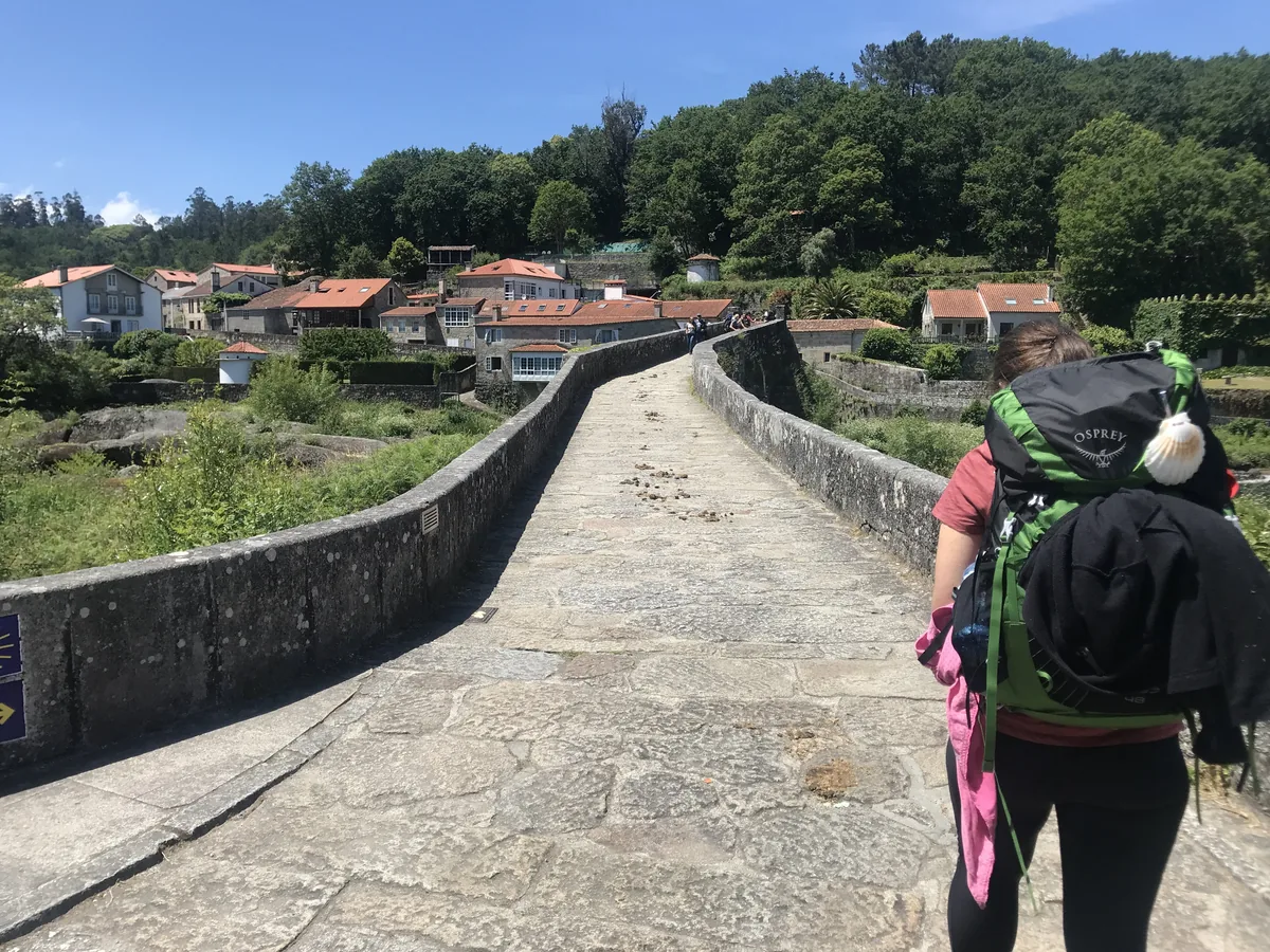 Pilgerinnen und Pilger überqueren eine alte Steinbrücke.
