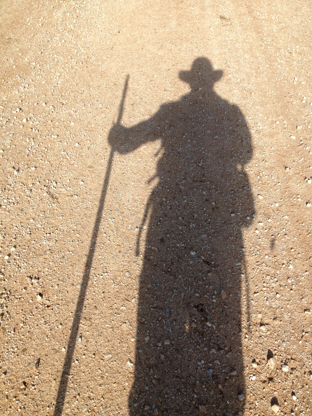 Schatten eines Pilgers mit Hut und Wanderstock auf dem Weg.