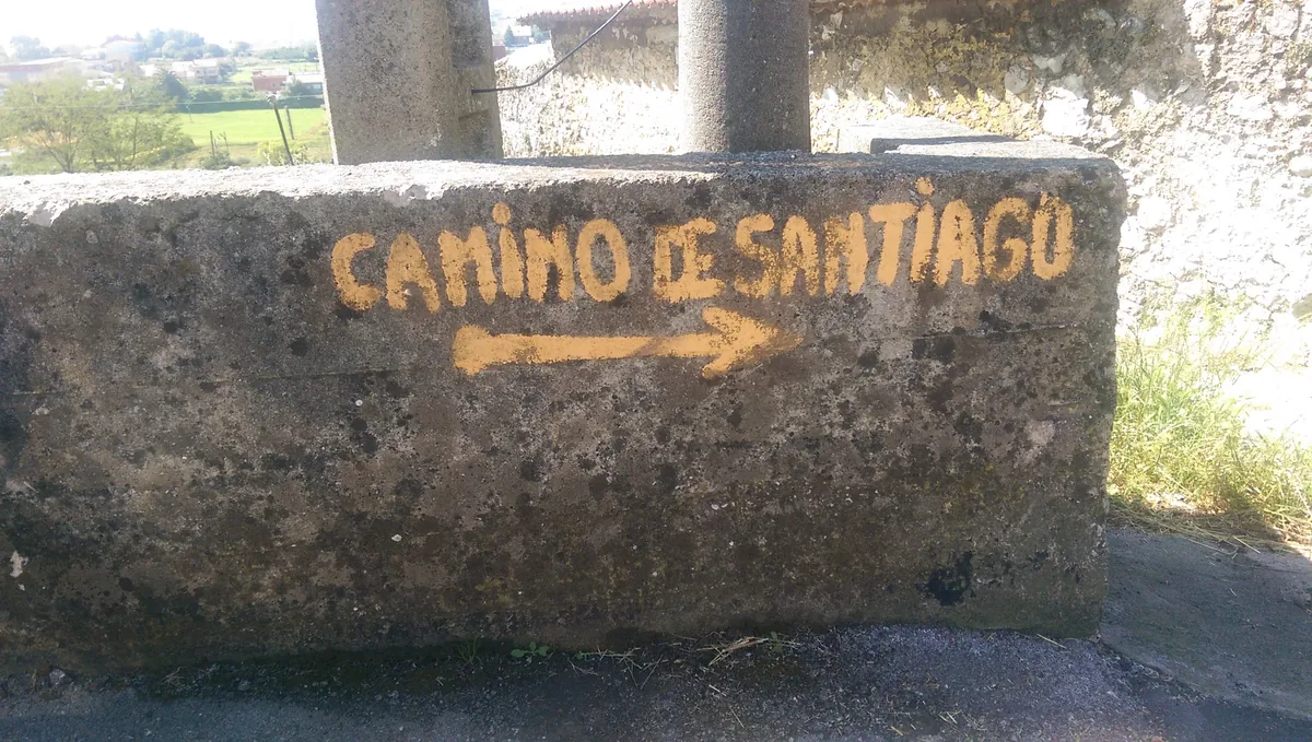 Handgemalter Schriftzug Camino de Santiago mit gelbem Pfeil an einer Mauer.