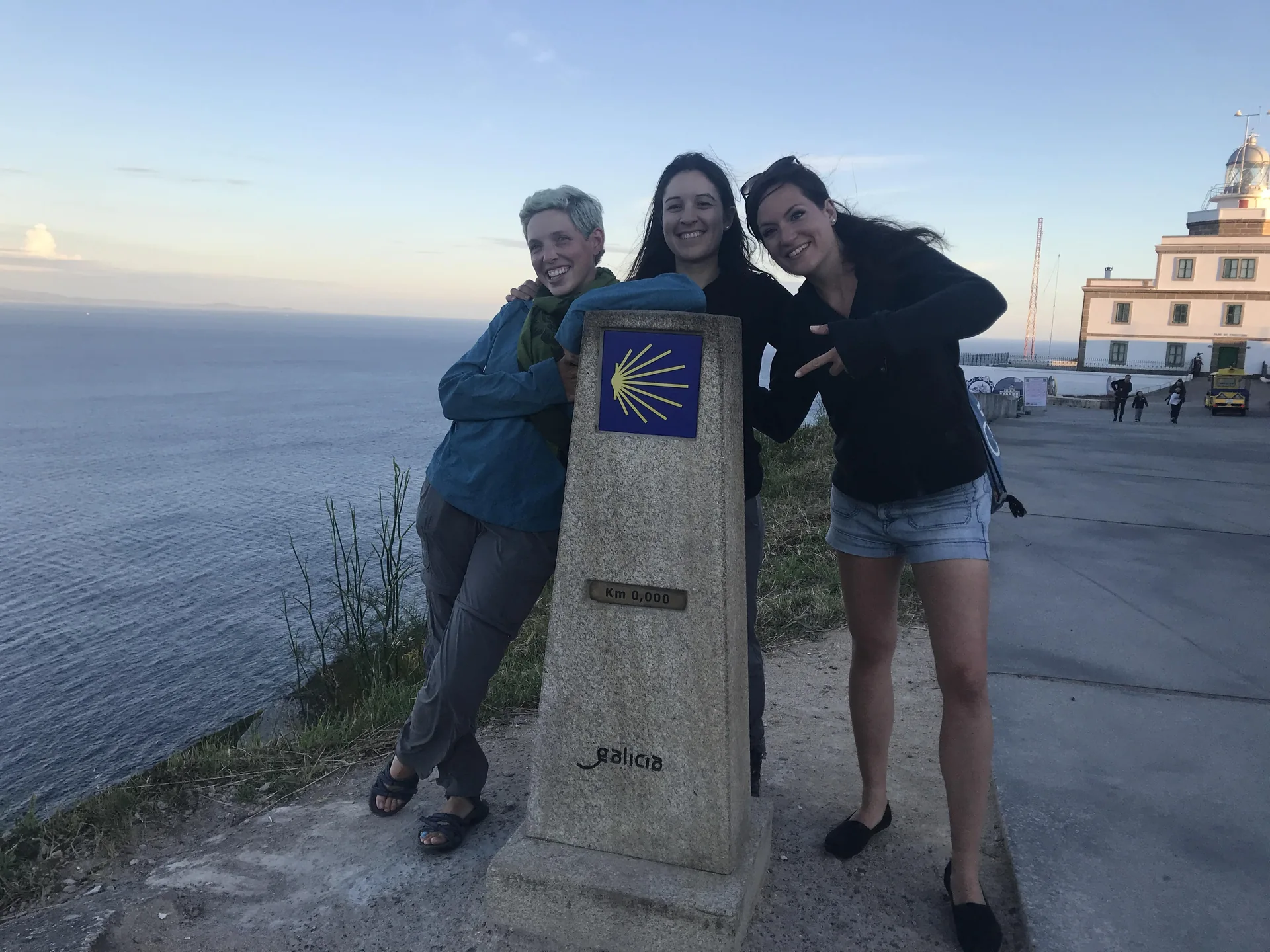 Sarah und ihre beiden Freundinnen am Kilometerstein in Finisterre.